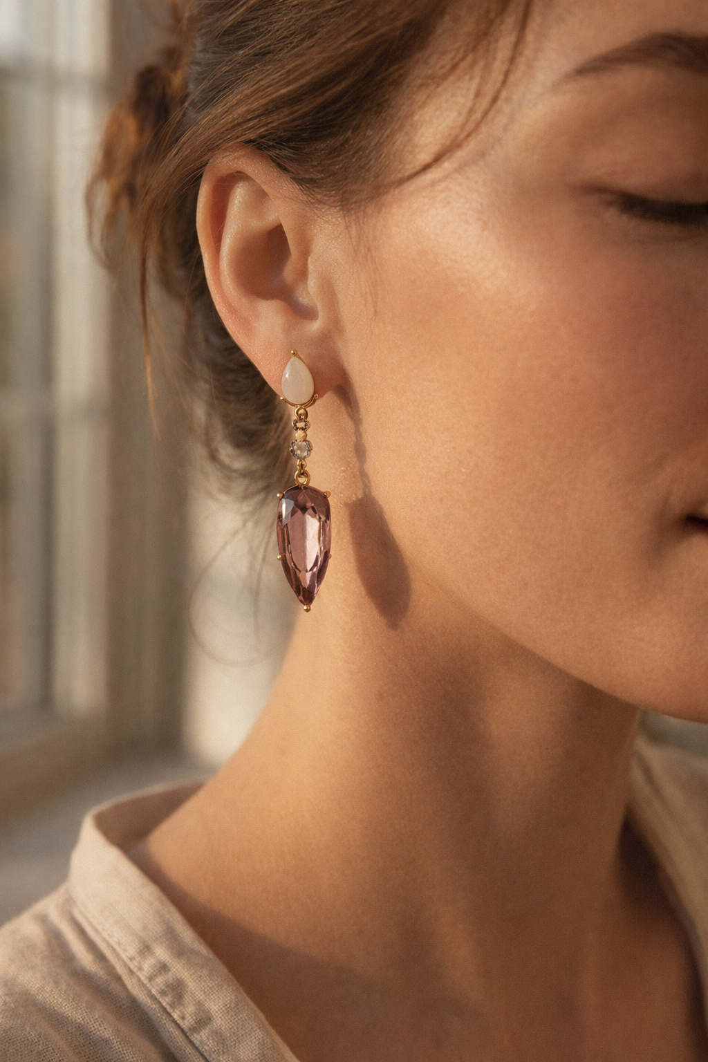 Close-up of a person wearing a dangling earring with a pink gemstone.