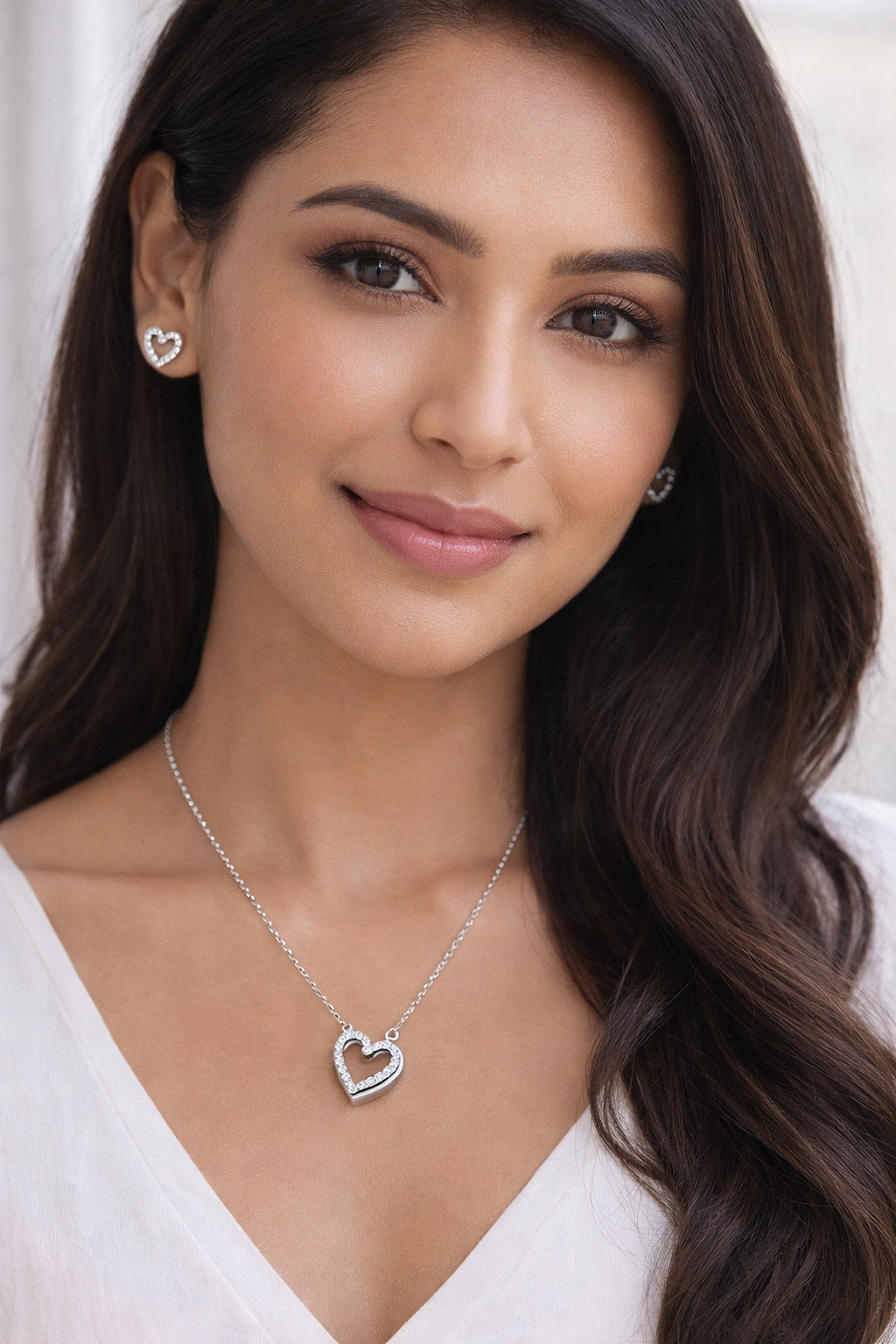 Woman wearing a silver heart-shaped necklace and earrings against a white background