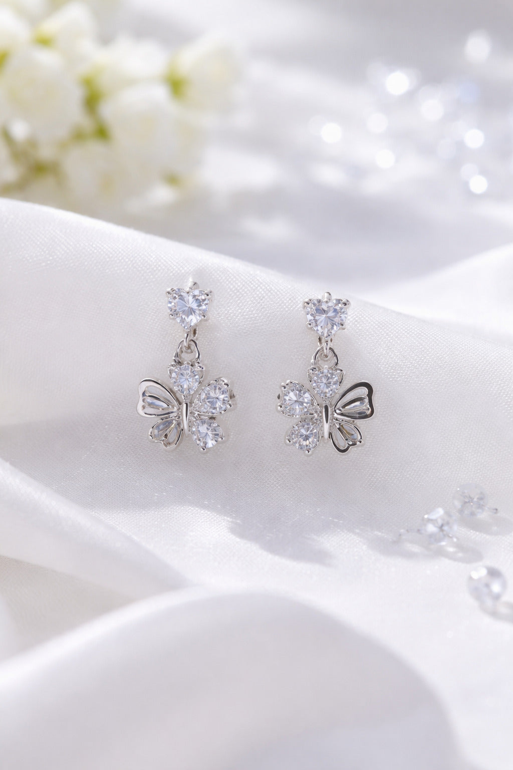 Butterfly-shaped earrings with clear stones on a white fabric background