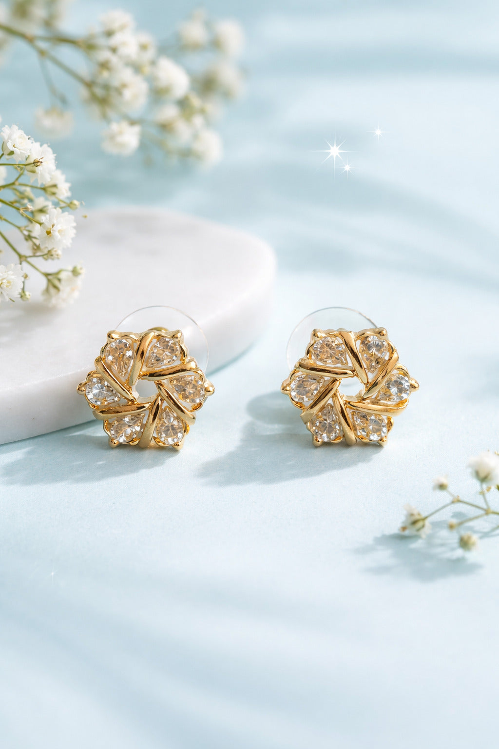 Gold earrings with diamond-like stones on a light blue background with white flowers.