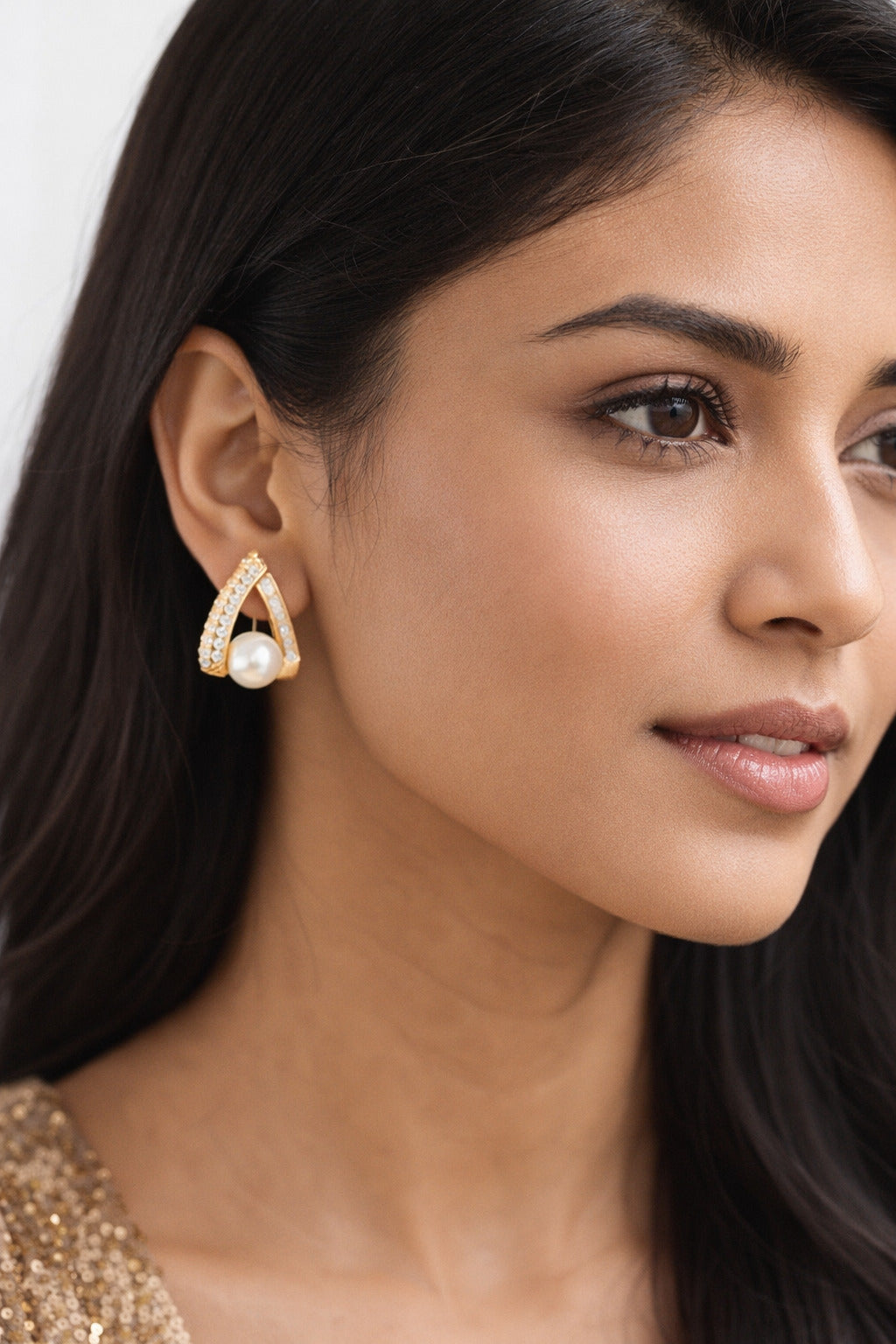 Close-up of a woman wearing a gold earring with a pearl accent.
