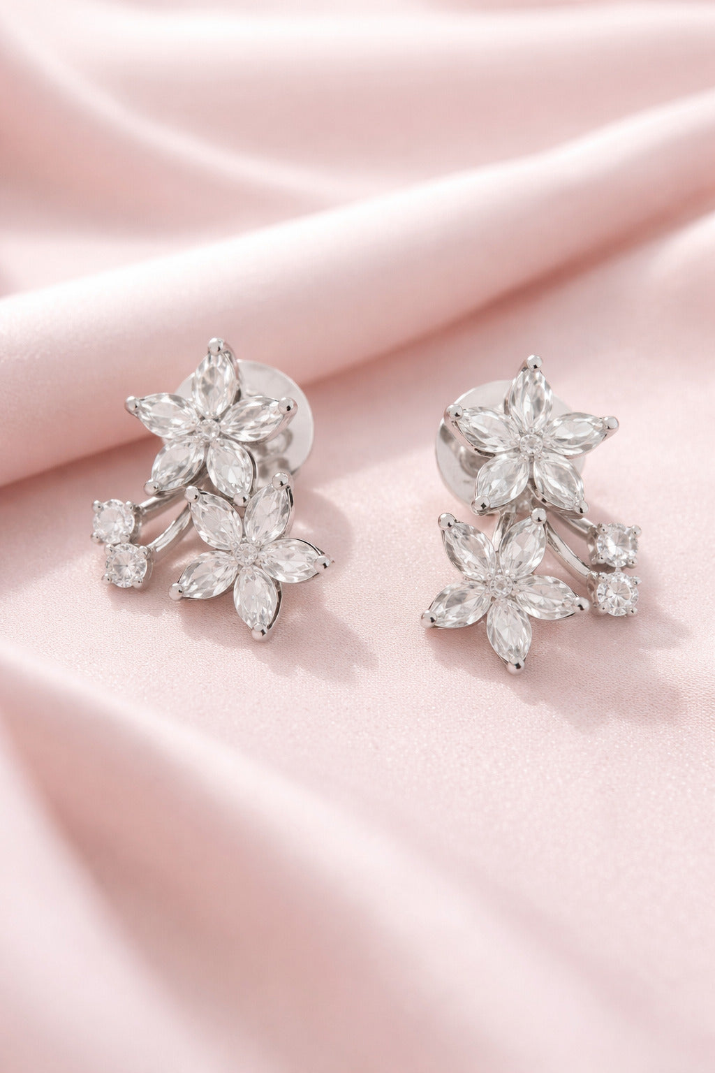 Silver floral earrings on a pink satin background
