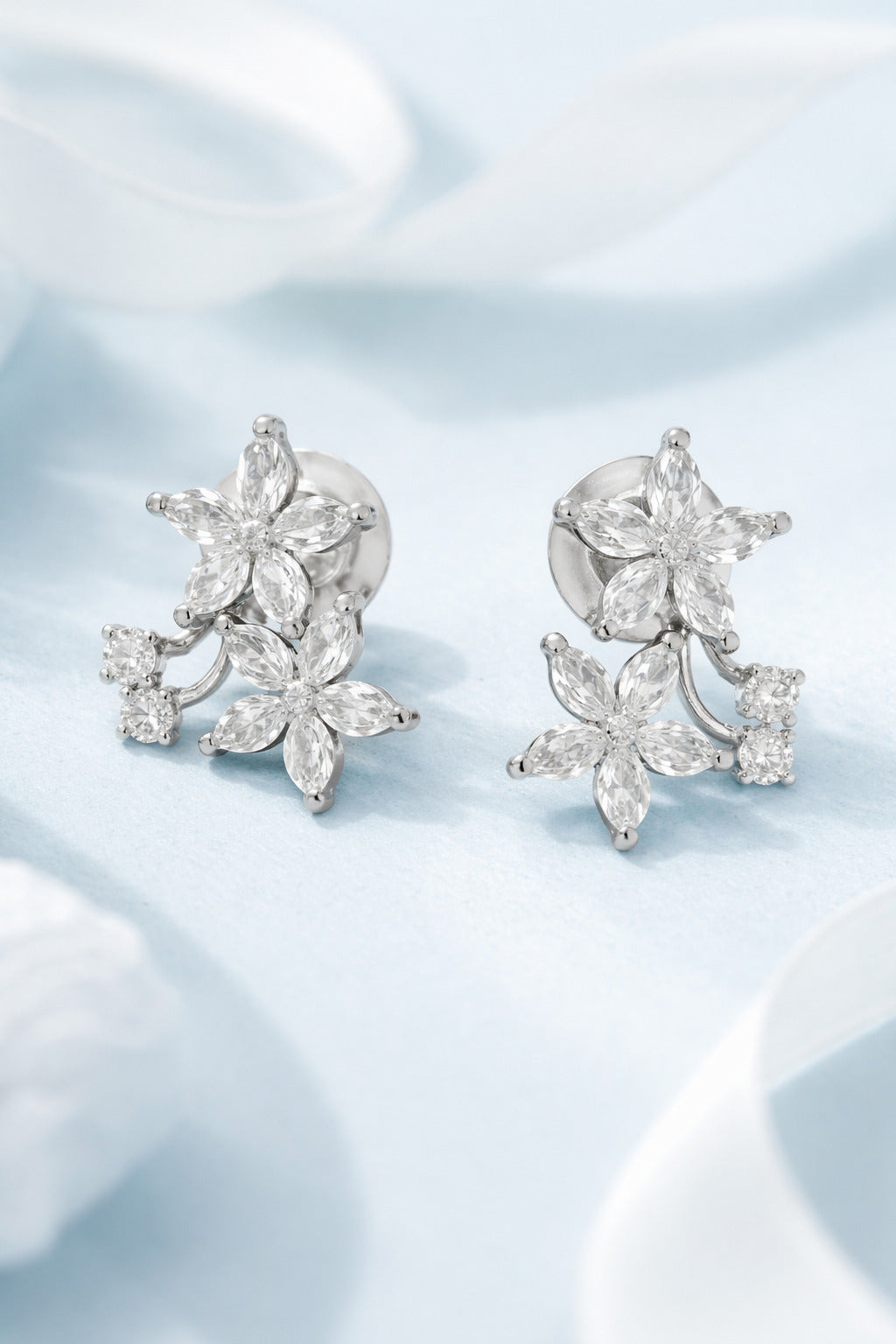 Pair of silver floral earrings with clear gemstones on a light blue fabric background