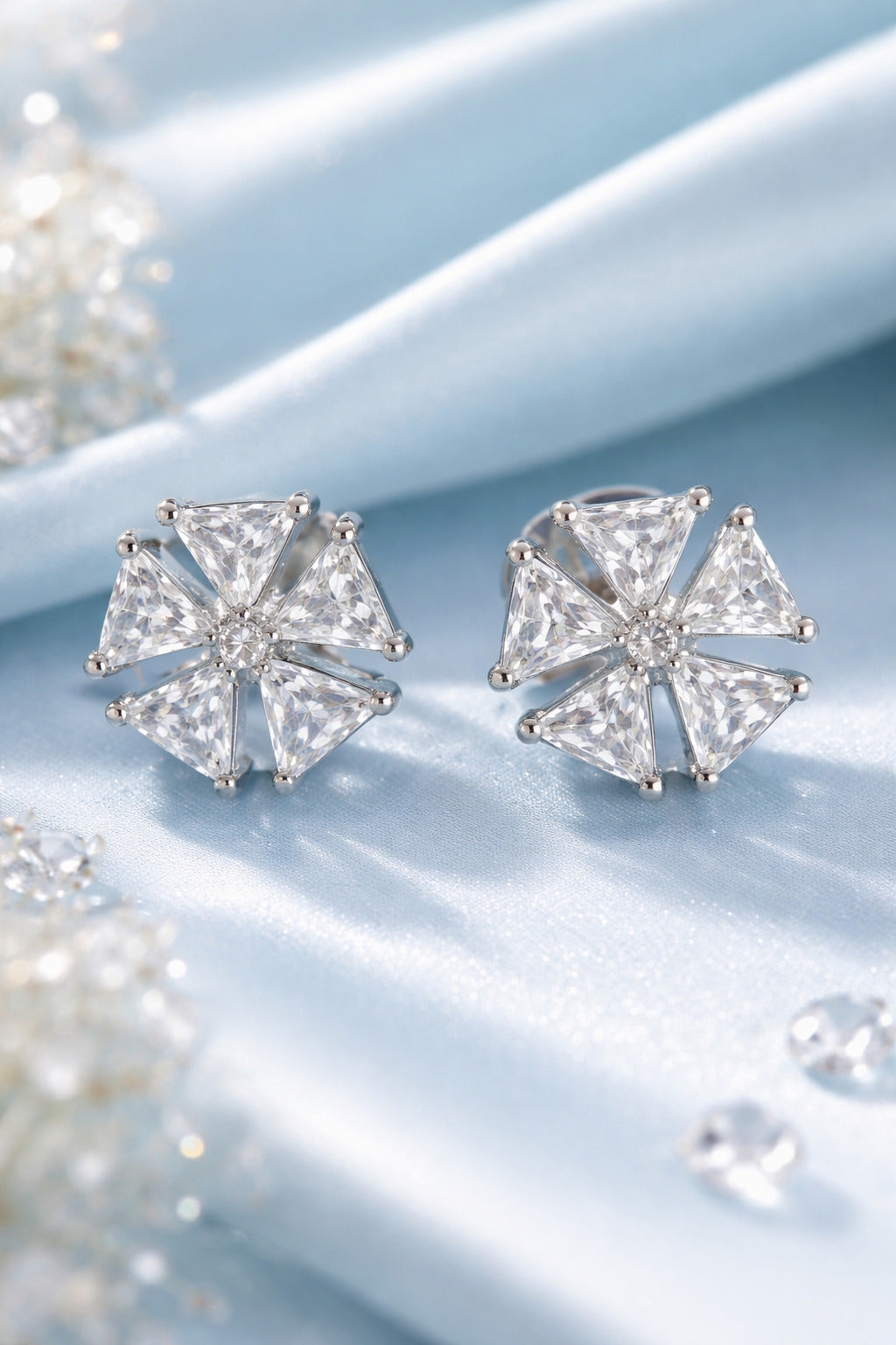 Pair of silver stud earrings with clear gemstones on a light blue surface.