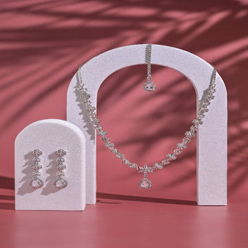 Silver necklace and earrings on a pink stand with a pink background