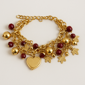 Gold bracelet with heart charm, red beads, and leaf-shaped pendants on a light background