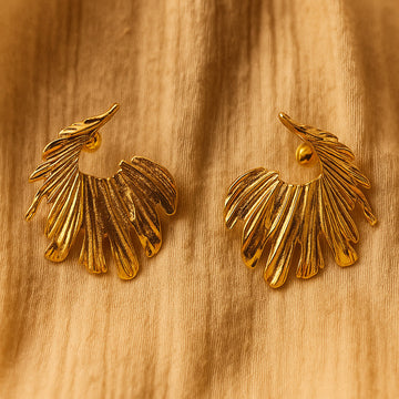 Pair of gold leaf-shaped earrings on a wooden surface
