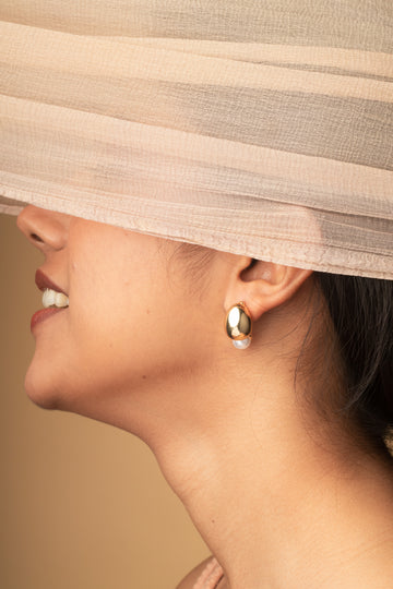 Close-up of a woman wearing gold hoop earrings with a beige headscarf.