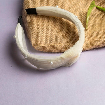 A white hair band with a soft elastic net and pearls, displayed on a textured background.