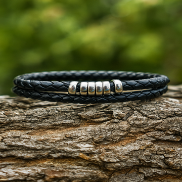 Black leather bracelet with silver beads on a wooden surface with a blurred green background