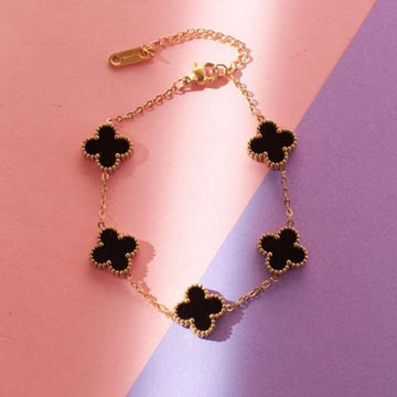 Gold necklace with black clover-shaped pendants on a pink and purple background