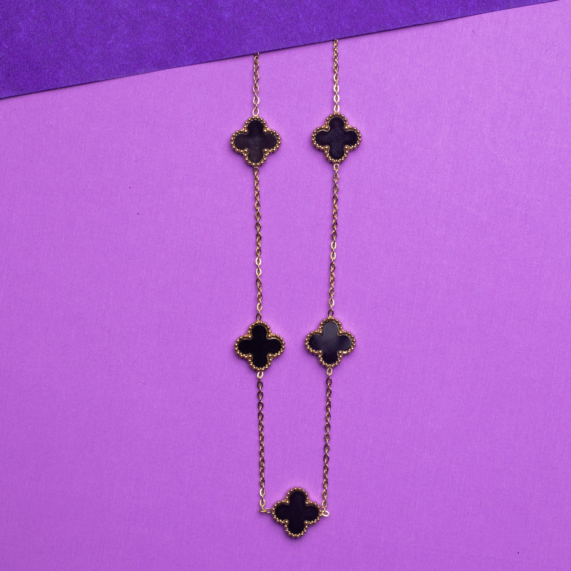 Long earrings with clover-shaped charms on a purple background