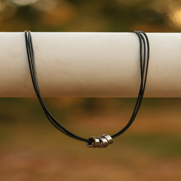 Black cord necklace with a silver clasp on a wooden stick against a blurred natural background