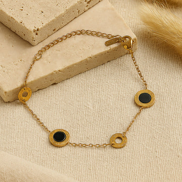 Gold bracelet with black circular charms on a beige stone surface