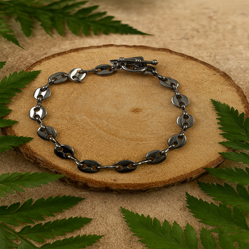 Silver chain bracelet on a wooden surface with green leaves