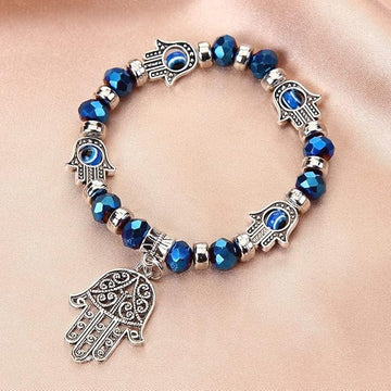 Bracelet with blue beads and silver Hamsa hand charms on a beige background