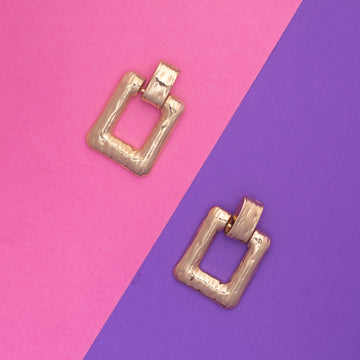 Gold square earrings on a pink and purple background