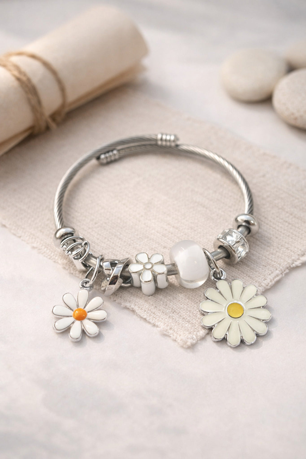 Silver bracelet with daisy flower charms on a light fabric background