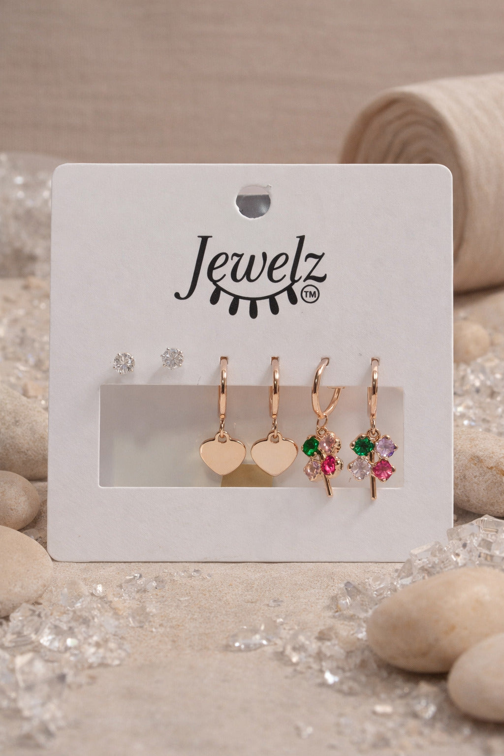 Set of earrings on a 'Jewelz' branded card with stones and sand in the background