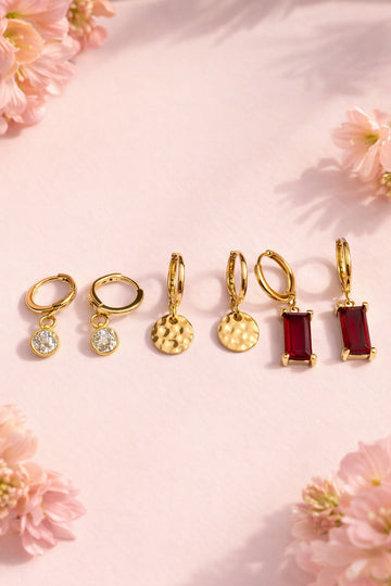 Set of gold and red earrings on a pink floral background