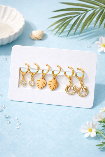 Set of gold earrings on a white card with a blue background and floral elements.