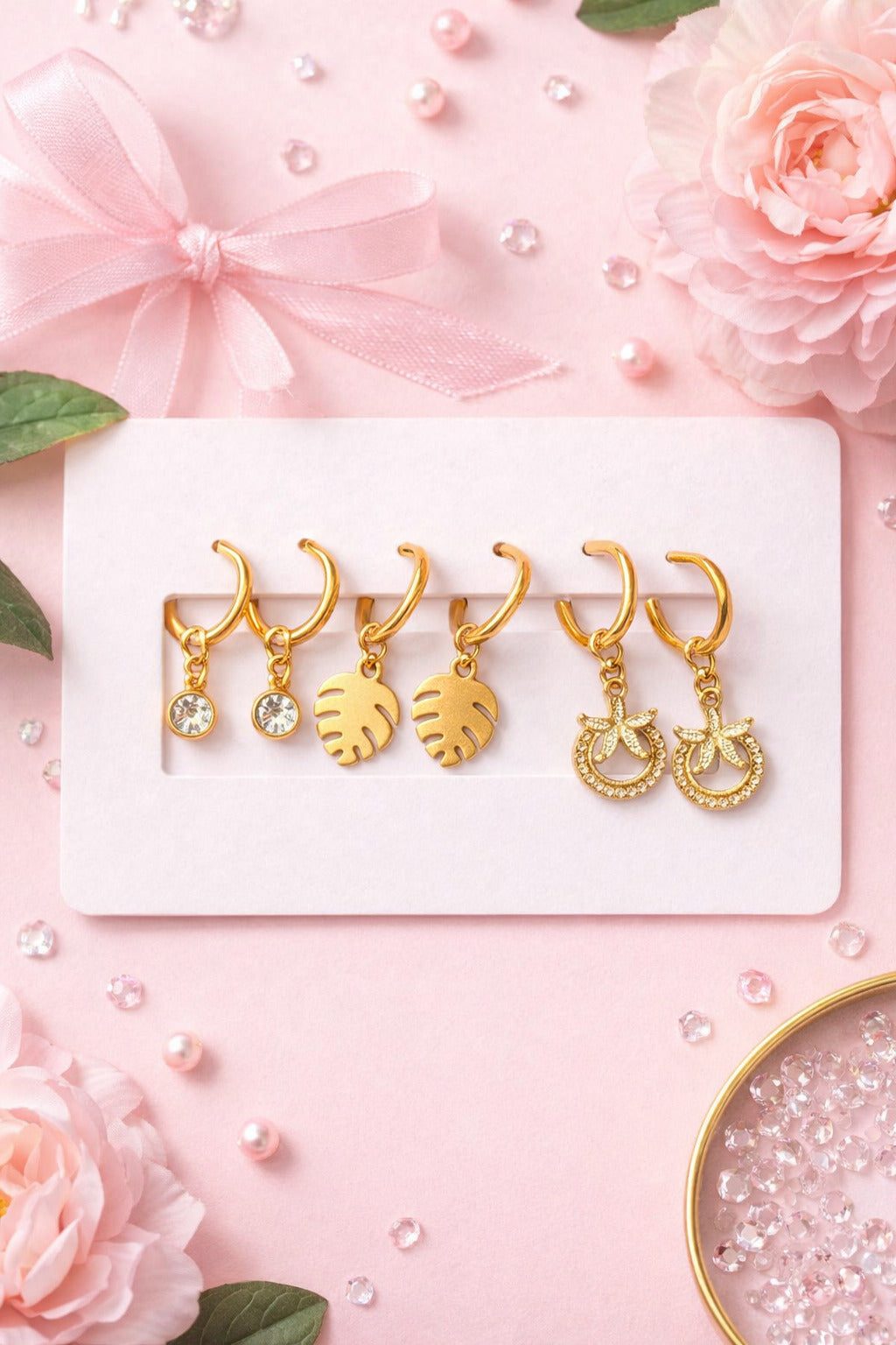 Set of gold earrings on a pink background with flowers and pearls