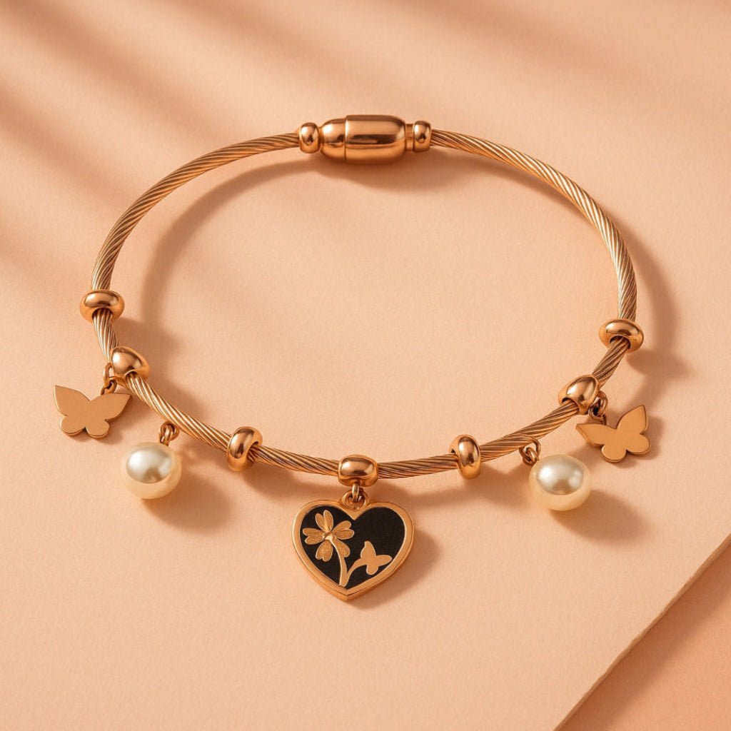 Gold bracelet with heart charm, butterfly, and pearl on a peach background