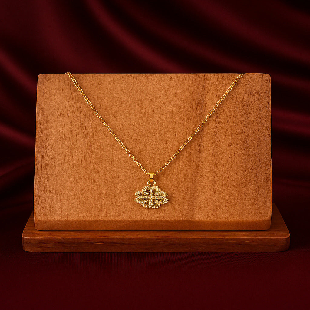 Gold necklace with a clover-shaped pendant on a wooden stand against a red curtain background