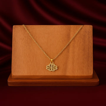 Gold necklace with a clover-shaped pendant on a wooden stand against a red curtain background