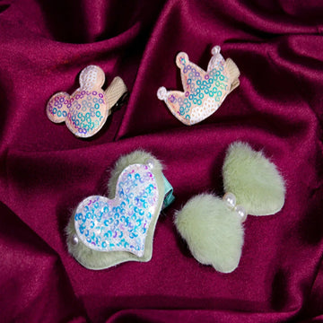 A collection of hair clips laid out on a purple fabric, featuring a heart shape, a flower shape, and some with glitter embellishments.