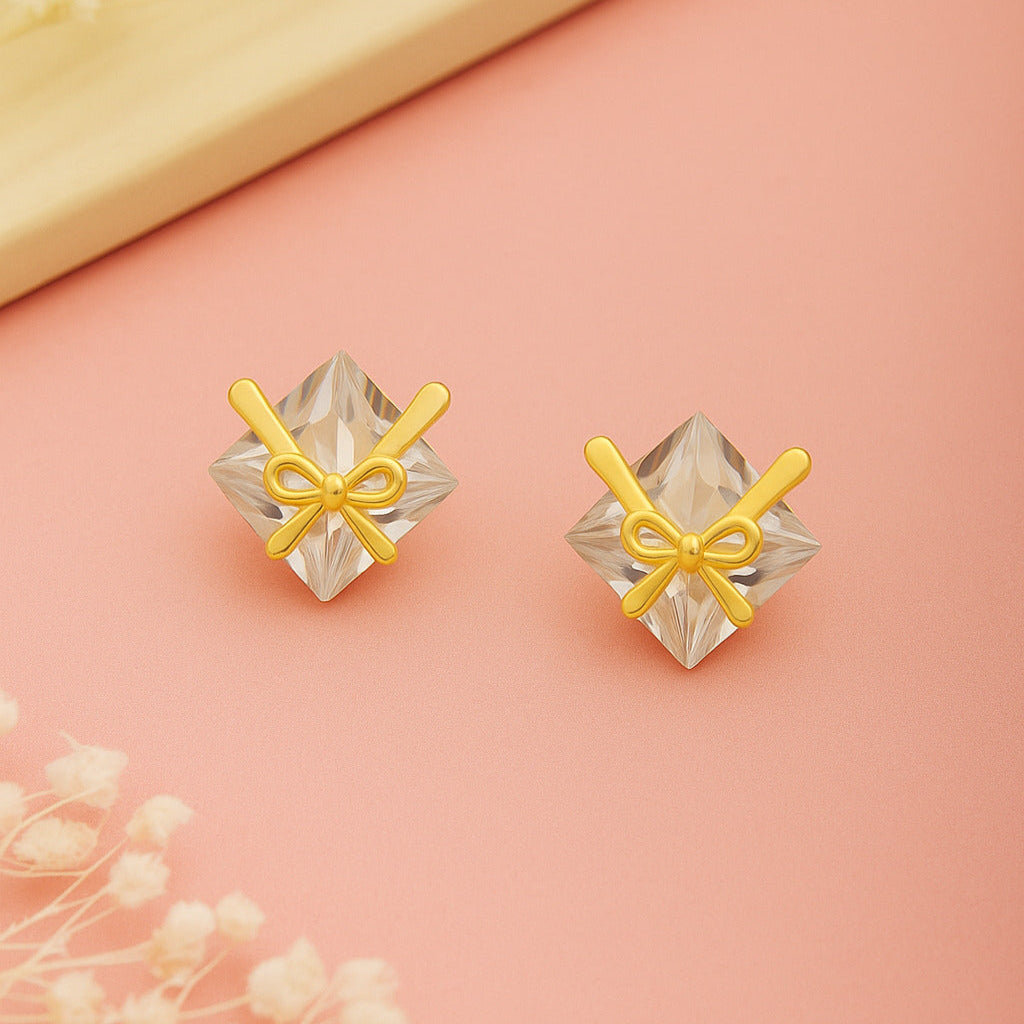 Diamond-shaped earrings with gold bows on a pink background
