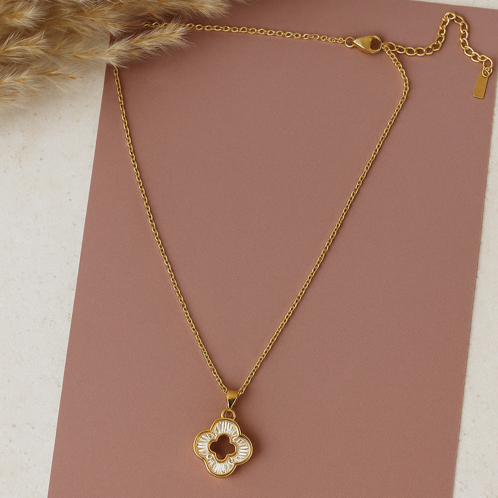 Gold necklace with a clover-shaped pendant on a brown surface