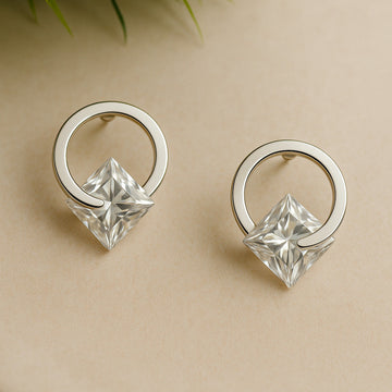 Silver earrings with clear gemstones on a beige background