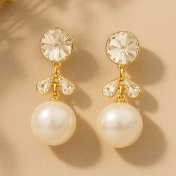 Pair of pearl earrings with gold accents on a beige background