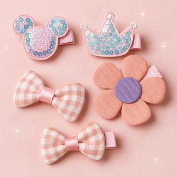Set of decorative hair clips including a crown, bow, and flower on a pink background