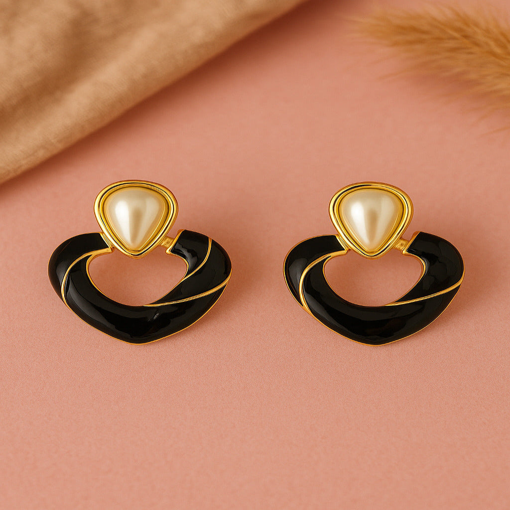 Pair of earrings with gold and black design on a pink background