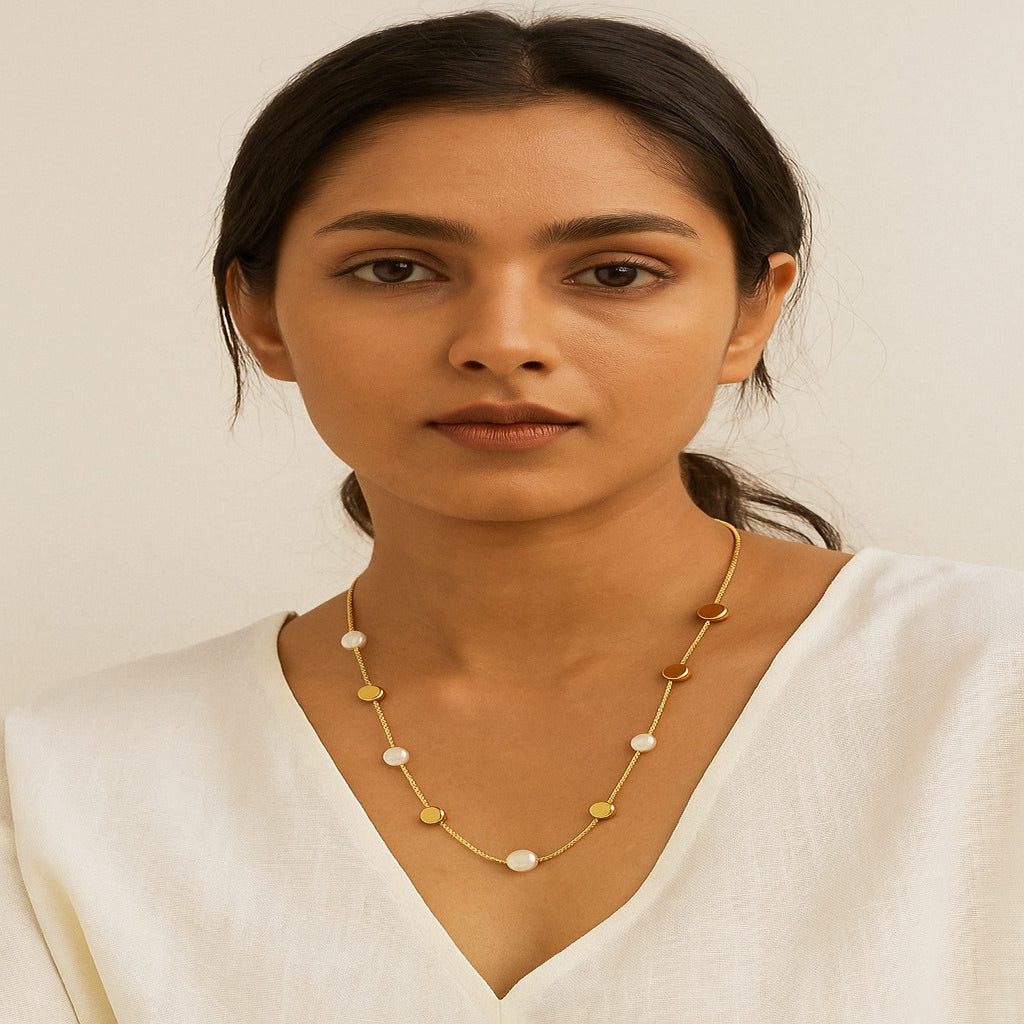 Woman wearing a gold necklace with small stones against a plain background