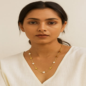 Woman wearing a gold necklace with small stones against a plain background