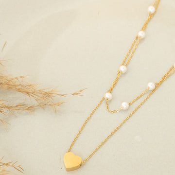Gold necklace with heart pendant and pearl strands on a light background