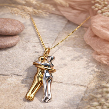 Gold and silver pendant of two people embracing on a chain against a natural background.