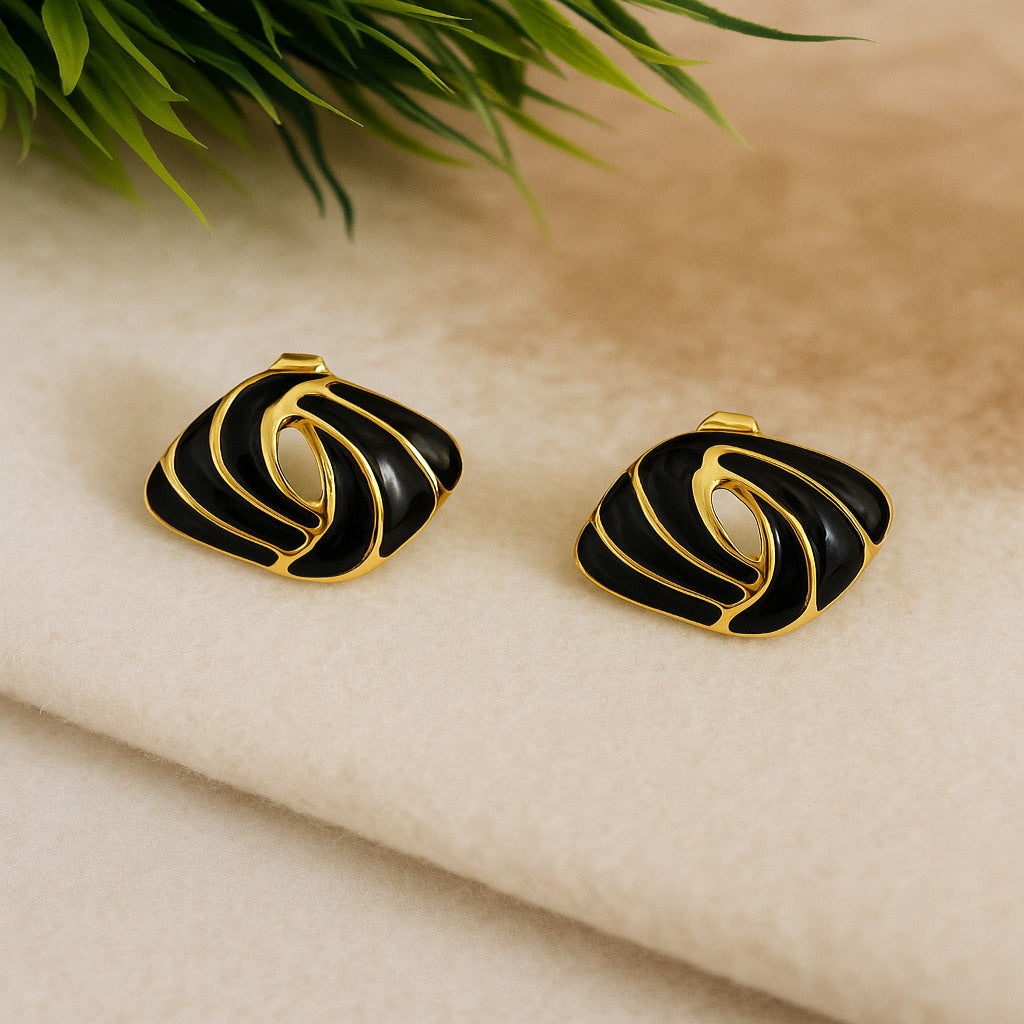 Black and gold earrings on a beige fabric background with green leaves.