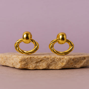 Pair of gold earrings on a stone surface with a pink background