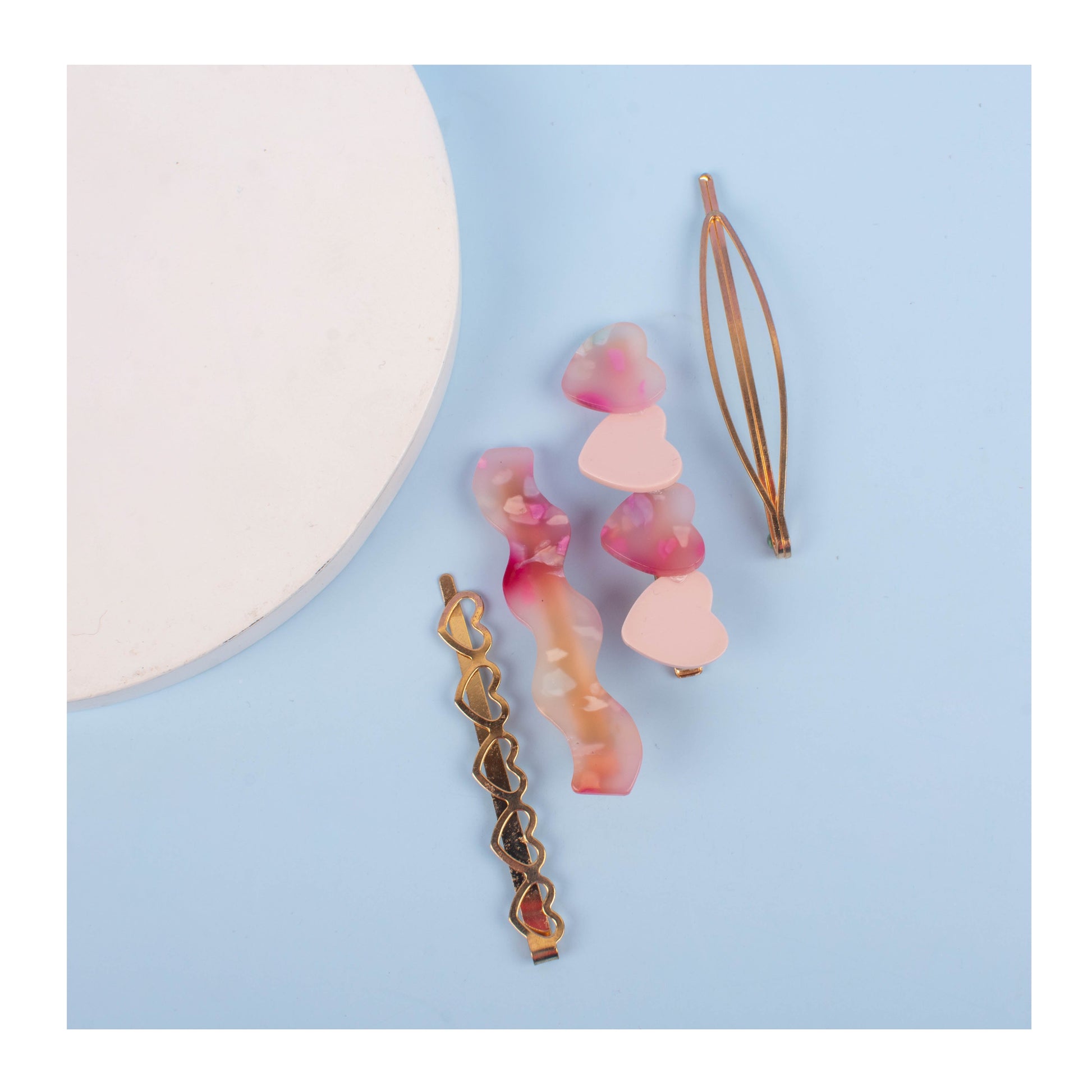 A collection of four hair clips laid out on a surface, featuring two with a pink heart design, one gold-colored, and one with a multicolor pattern.