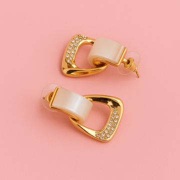 Gold and beige earrings on a pink background