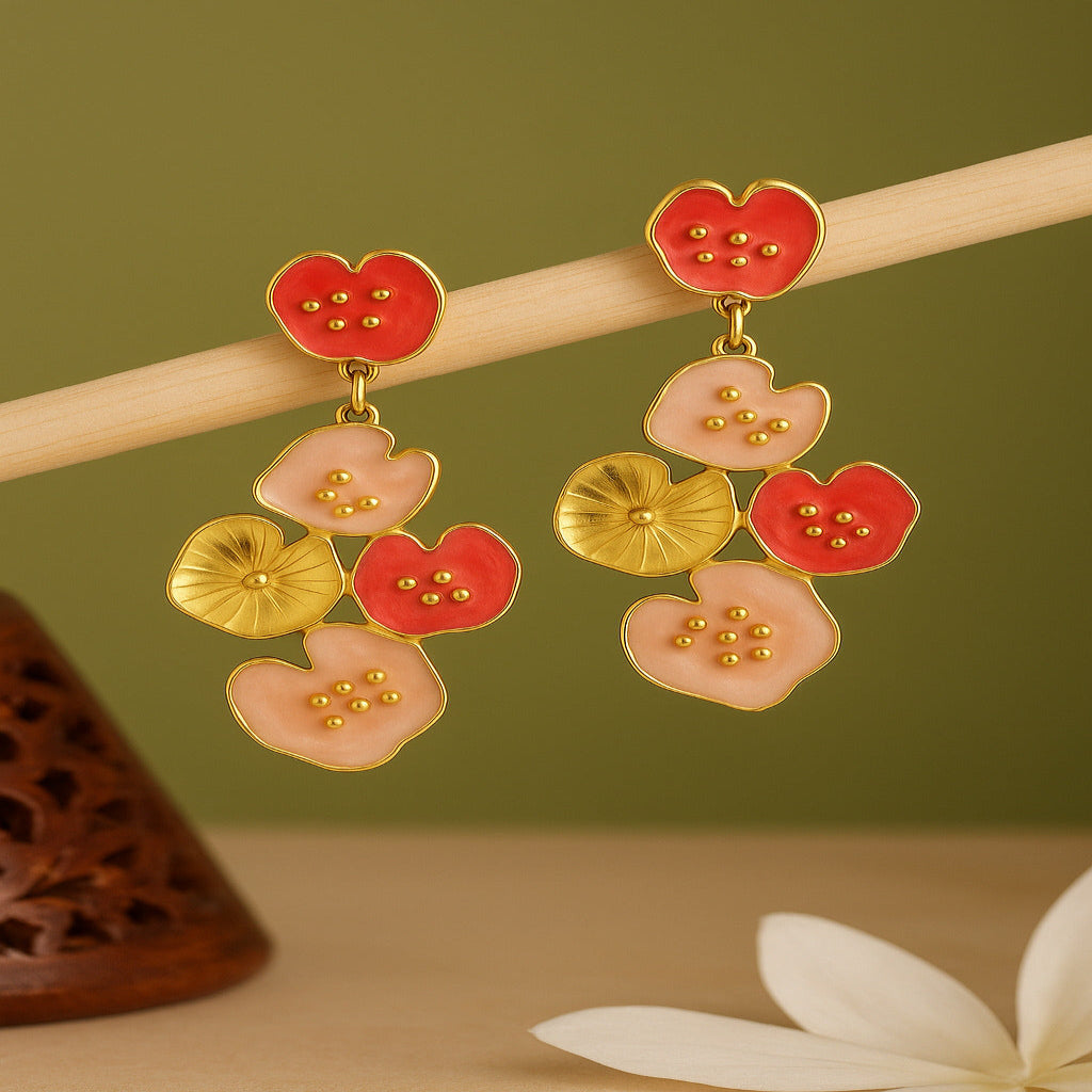 Floral earrings with red, pink, and gold colors on a wooden stick against a green background.