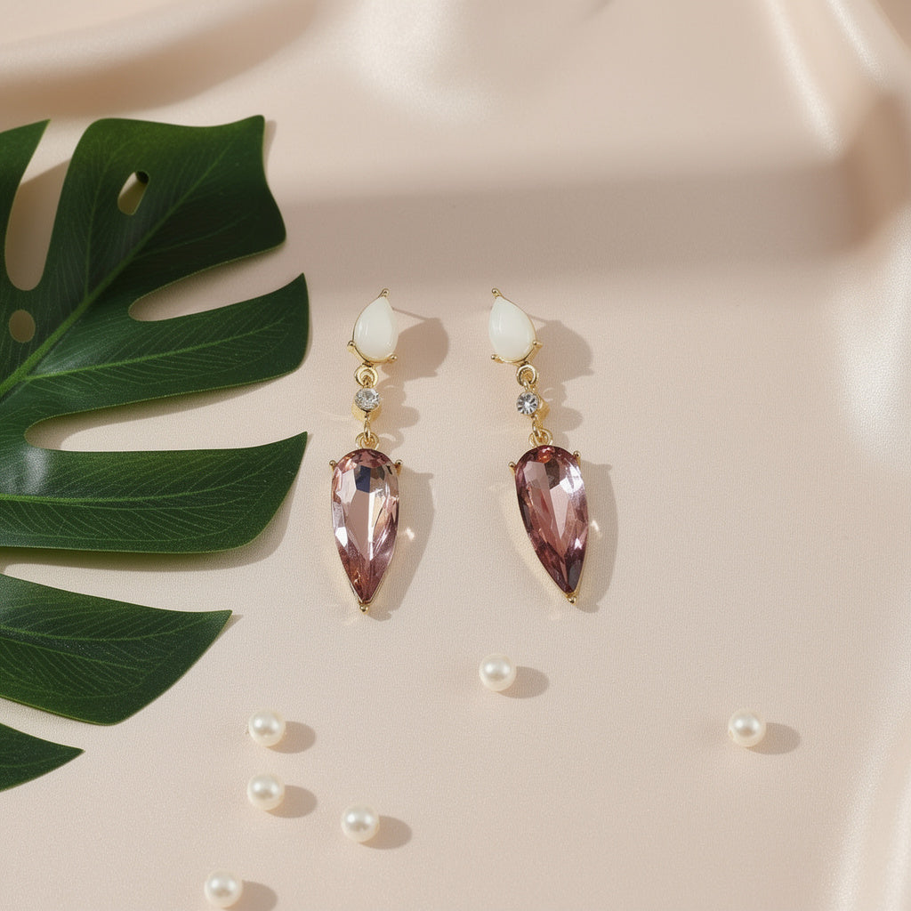 Pair of earrings with teardrop-shaped gemstones on a beige surface with pearls and a leaf.