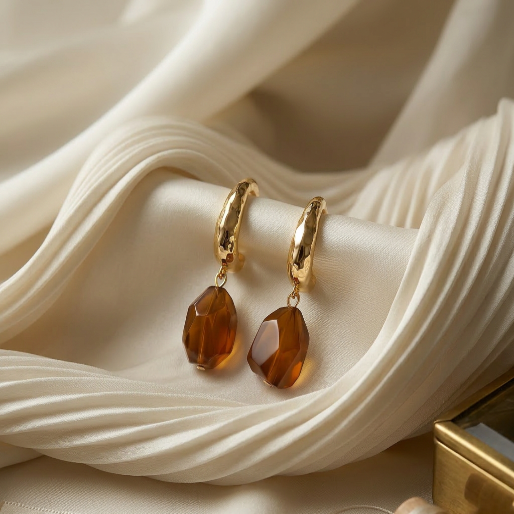 Gold earrings with brown gemstones on a beige fabric background