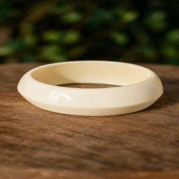 White bangle on a wooden surface with a blurred green background