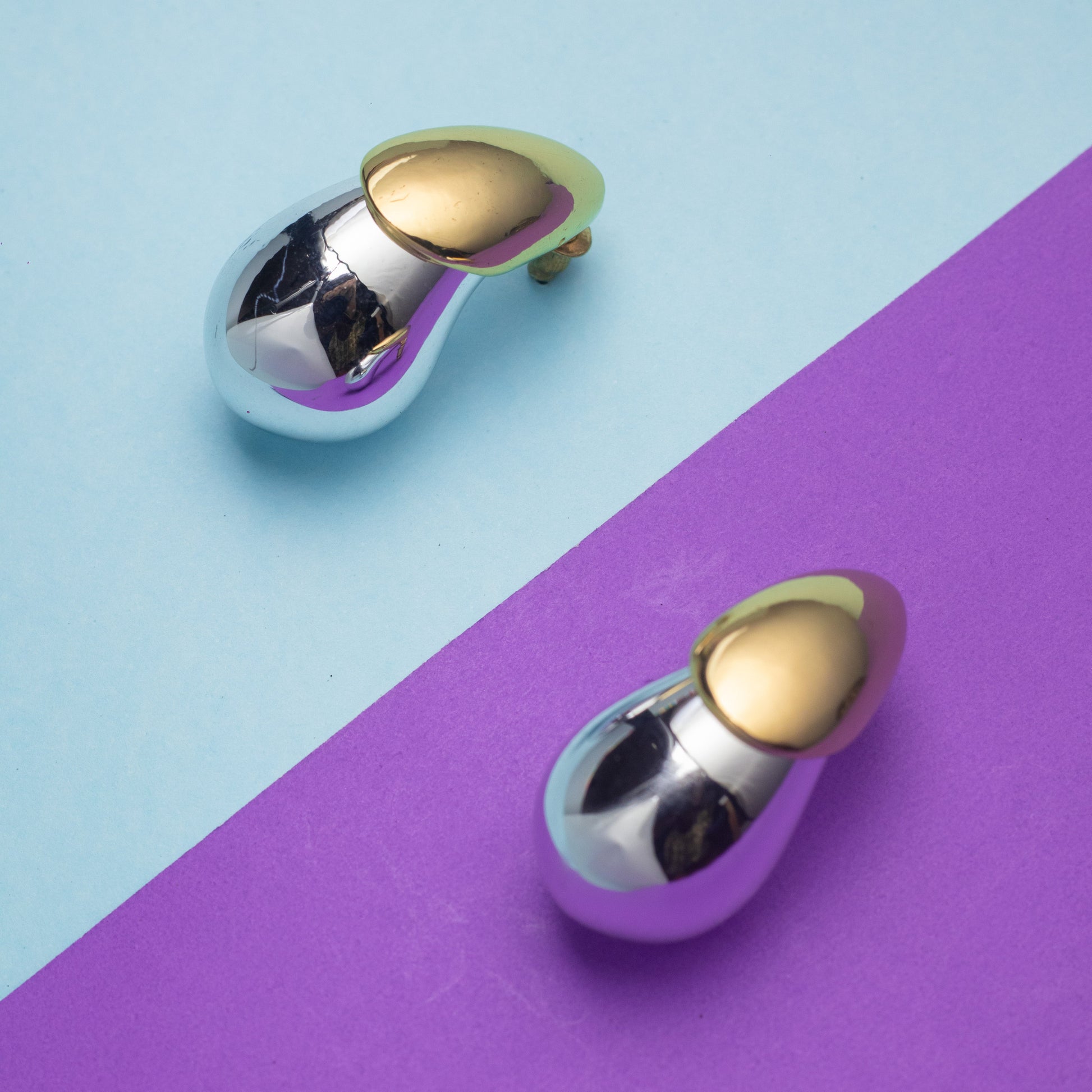 Pair of gold and silver earrings on a two-tone blue and purple background