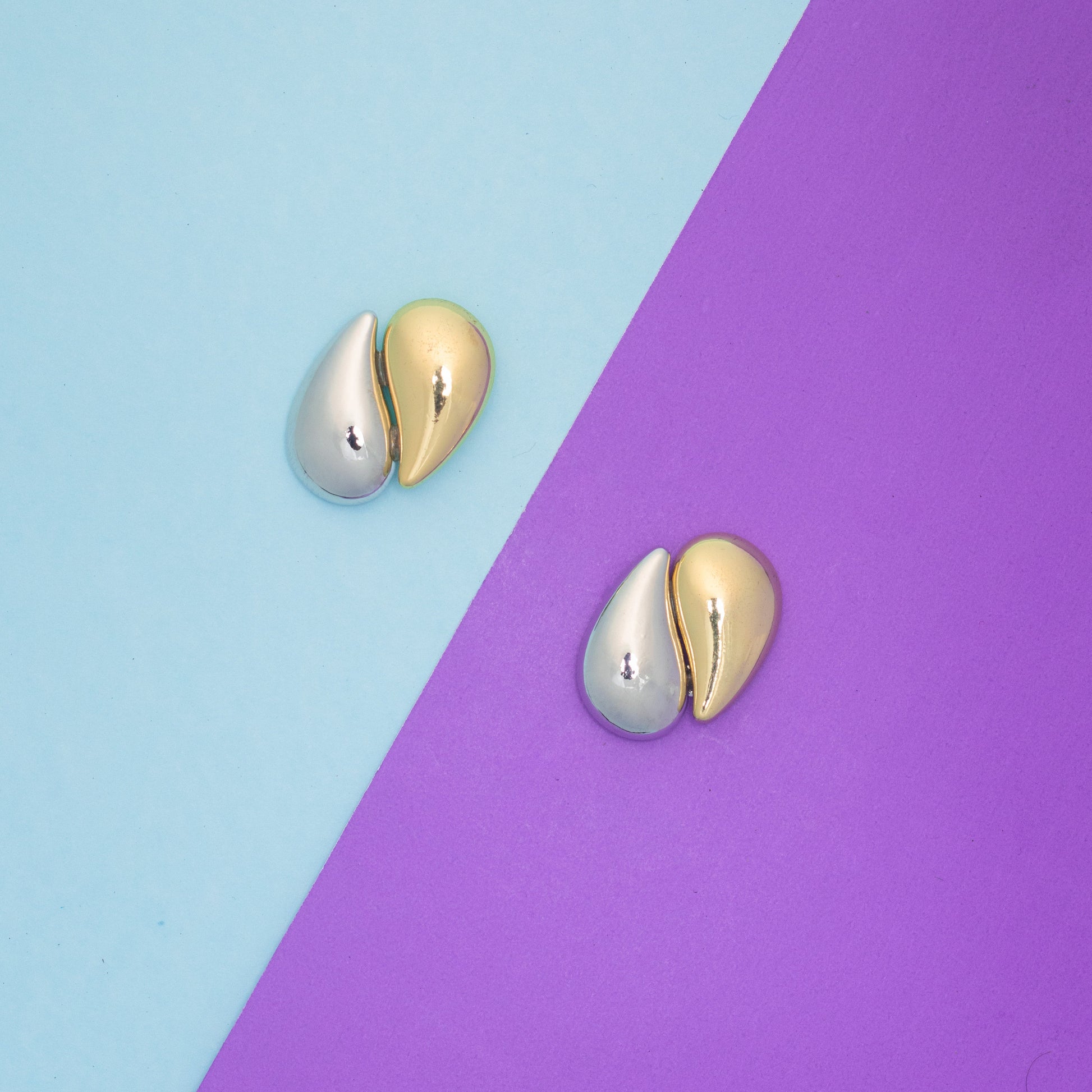 Gold and silver earrings on a two-tone blue and purple background